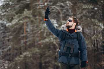 Bearded hiker in blue parka and mirrored sunglasses making selfie in a winter forest