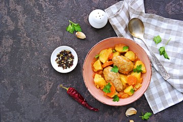 Hearty stew with potatoes, carrots and chicken meat balls in a pink bowl on a dark concrete background. Copyspace. Top view.