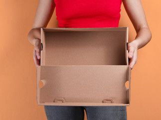 Young woman holding empty cardboard box on orange background. Crop photo, studio shot