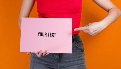 Woman holding pink empty sheet of paper for copy space on orange background. Crop photo, studio shot
