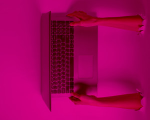 Female hands holding a laptop through the torn holes with pink neon light. Creative business art