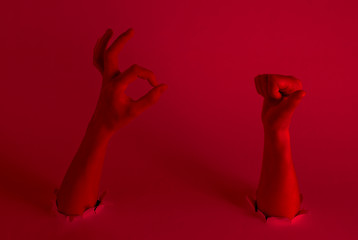 Female hands show thumb up and ok symbol through torn holes with red neon light. Creative art. Pop culture
