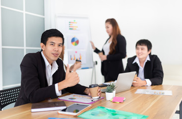 smart asian man officer typing report with laptop, he prepare information to executive conference and show thumb up sign, leadership and organization management, asian officer team discuss together