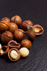 Whole and open macadamia nuts with key on black background.
