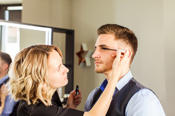 Professional actor preparation before shoot. Handsome young man applying by professional make up of visagist.