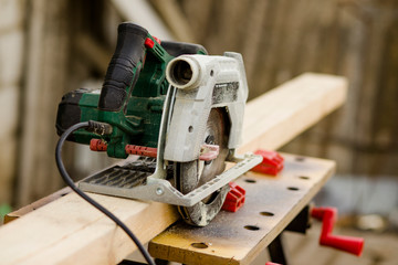 A modern green circular saw lies on a wooden table in the workshop. Closeup of a circular saw