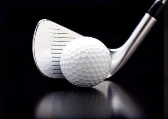 Closeup of a nine iron with a golf ball on black with reflection.