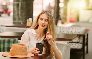 Cheerful smiling blond woman sits in a street cafe and drinks coffee