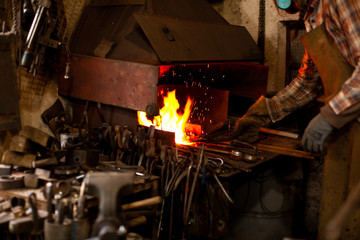 The blacksmith manually forging the molten metal on the anvil in smithy.