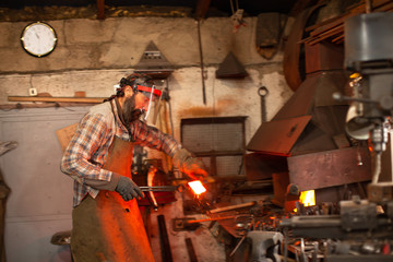 Real brutal blacksmith works in a workshop with a red-hot iron.