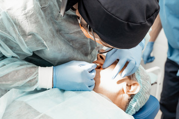 Patient and dentist during implant placement operation. Real operation. Tooth extraction, implants. Professional uniform and equipment of a dentist. Healthcare Equipping a doctor’s workplace.