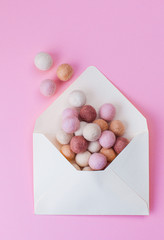 Minimal composition with felt balls flying out from opened envelope over pink background
