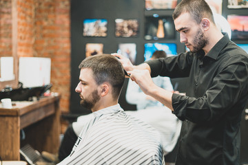 Haircut at the hairdresser. Barber cuts the hair on the client's head. The process of creating hairstyles for men. A man in a barbershop. The near plan. Equipment stylist. Selective focus