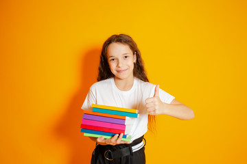 School girl holding stack of books over yellow background. Happy girl in school uniform showing ok sign.
