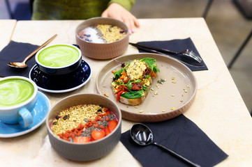 raw healthy food breakfast. smoothie bowl, toast with hummus, and matcha latte green tea cup on the...