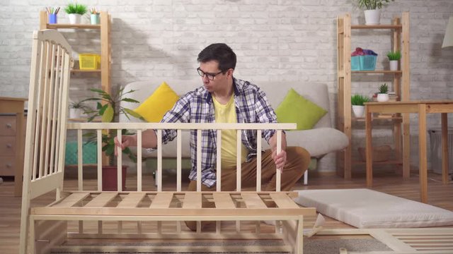 positive young man future father collects a child's bed in the bedroom