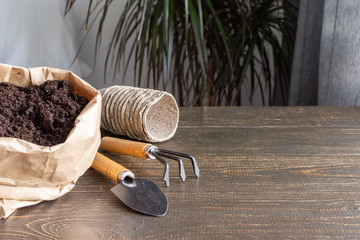 Eco friendly pots for seedlings on wooden background, small bag with ground and garden trowel and...