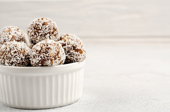 Energy balls of dates, nuts, oats, sprinkled with coconut powder closeup in a white plate on a white background background with copy space