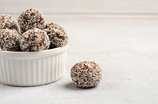 Energy balls of dates, nuts, oats, sprinkled with coconut powder closeup in a white plate on a white background background with copy space