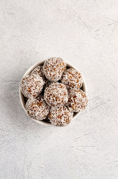 Energy balls of dates, nuts, oats, sprinkled with coconut powder closeup in a white plate on a white background background with copy space with place for text.