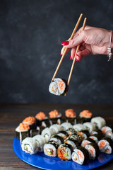 Beautiful female hands take sushi with chopsticks. Dark background. Wooden plank. Side view. Horizontal view Blue plate. Sushi. Assorted