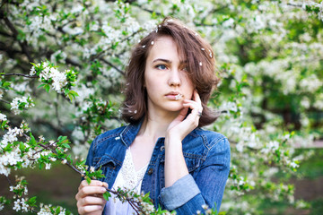 Lovely girl in a denim jacket on a background of flowering trees. Romantic picture. Spring is a sunny day.