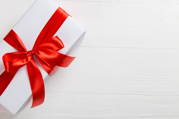 White packed gift with red ribbon on the table. Romantic surprise on holiday for a loved one.