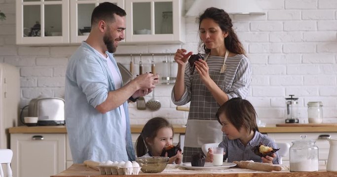 Young couple enjoying fresh homemade muffins with smiling kids.