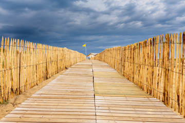 Heller, hölzener Strandübergang in Lacanau Océan, Frankreich, bei aufziehenden, dunklen Gewitterwolken