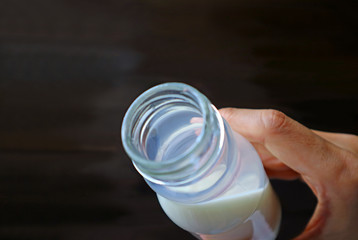 Man's hand holding opened bottle of milk on dark brown background