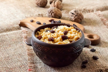 Fototapeta na wymiar Sweet millet porridge with dark raisins in ceramic rustic bowl