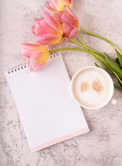 Cup of coffee, notebook and pink tulips top view on marble background
