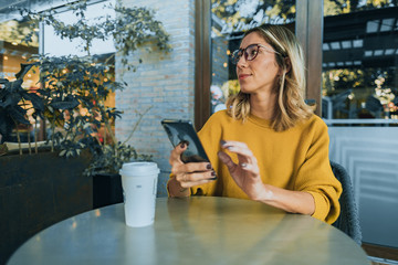Mujer tomando café en starbucks con celular en mano samsung - obrazy, fototapety, plakaty