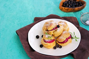 Dessert, choux pastry with cream of cream cheese and blackcurrant berry mousse on a white plate on a turquoise concrete background. Berry Cream Desserts recipe