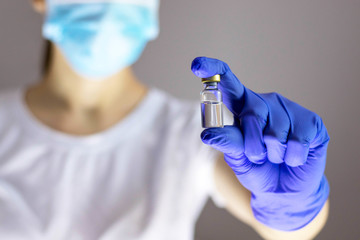 Doctor in protective gloves and mask holding glass vial with injection liquid. Vaccination against influenza and coronavirus. Hospital nurse. Health care concept. Medicine bottle.