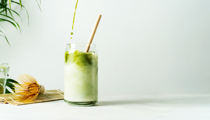 Making Japanese iced matcha latte, green tea with milk, soy milk, traditional matcha tools, with bamboo straw in glass on white background. - obrazy, fototapety, plakaty