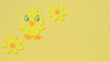 felt crafted chick and flowers for easter on a yellow             background with writing space