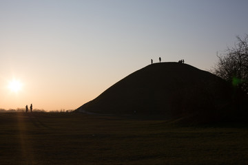 People silhouetted against the sky, watching the sun set from a hill in Krakow, Poland