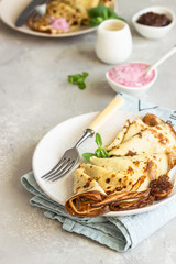 Crepes, thin pancakes with pink yogurt, jam and honey decorated with mint on a ceramic plate. 