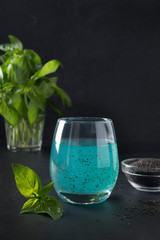 Tropical blue cocktail with basil seeds in glass on black. Close up. Vertical. Detox and freshness.