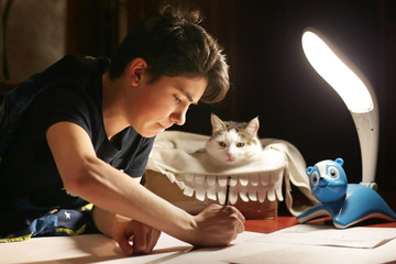 boy architect student working on drafting project in night with cat in box beside