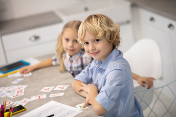 Two blond kids putting cards with letters on the table and looking contented