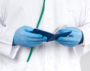 doctor in a white coat and blue gloves holds a blue paper notebook for notes