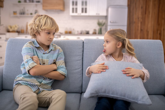Blond cute girl with a pillow showing tongue to her brother