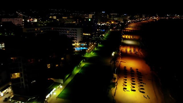 Aerial over the beachside during the night. View of light projecting on the beach loungers.