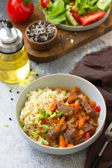 Healthy eating concept. Beef stewed with vegetables in bulgur sauce and fresh vegetable salad on a light stone table top.