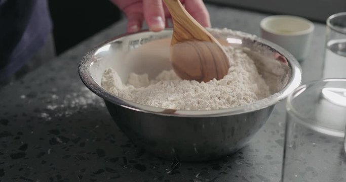 Slow motion man mixing dry ingredients with flour in steel bowl on concrete countertop