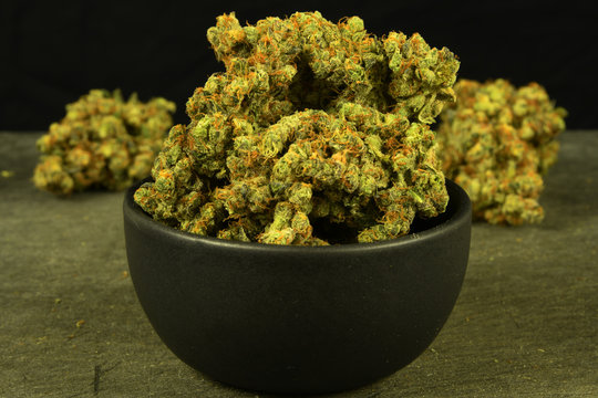 Marijuana buds in black bowl on gray board with black background