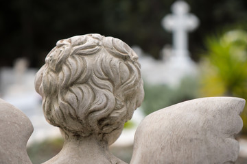 Back view of an Angel looking towards a marble cross in a graveyard