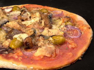 Pizza with sardines, tomatoes and olives on a thin dough.On black background